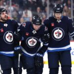 Apr 13, 2025; Winnipeg, Manitoba, CAN; An injured Winnipeg Jets defenseman Dylan Samberg (54) is taken of the ice during a game against the Edmonton Oilers with the help of Winnipeg Jets defenseman Dylan DeMelo (2) and Winnipeg Jets center Morgan Barron (36) in the second period at Canada Life Centre. Mandatory Credit: James Carey Lauder-Imagn Images