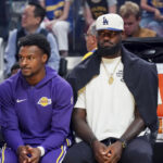 Oct 5, 2025; San Francisco, California, USA; Los Angeles Lakers guard Bronny James (9) and forward LeBron James (23), wearing a Los Angeles Dodgers cap, watch the action against the Golden State Warriors in the first quarter at Chase Center. Mandatory Credit: David Gonzales-Imagn Images