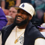 Oct 5, 2025; San Francisco, California, USA; Los Angeles Lakers forward LeBron James (23), wearing a Los Angeles Dodgers hat, smiles after watching his son, guard Bronny James (9), dunk a rebound against the Golden State Warriors in the third quarter at Chase Center.