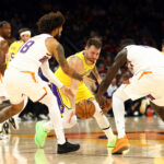 Oct 14, 2025; Phoenix, Arizona, USA; Los Angeles Lakers guard Luka Doncic (77) reaches for a loose ball against Phoenix Suns center Khaman Maluach (10) and forward Isaiah Livers (18) during an NBA preseason game at Mortgage Matchup Center.