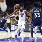 Oct 17, 2025; Philadelphia, Pennsylvania, USA; Philadelphia 76ers center Joel Embiid (21) drives the lane between Minnesota Timberwolves guard Rob Dillingham (4) and forward Leonard Miller (33) during the third quarter at Xfinity Mobile Arena.