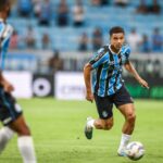 Zagueiro canhoto Viery com a bola em jogo do Grêmio, com André Henrique desfocado na imagem