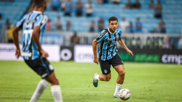 Zagueiro canhoto Viery com a bola em jogo do Grêmio, com André Henrique desfocado na imagem