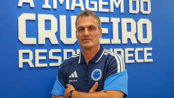 Executivo de futebol Bruno Spindel com a camisa do Cruzeiro, com um fundo azul atrás com os dizeres "a imagem do Cruzeiro resplandece" em letra bastão