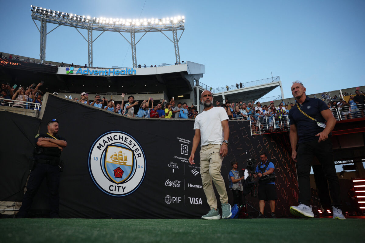 Técnico Pep Guardiola entrando em campo -há do lado esquerdo uma bandeira do Manchester City com fundo preto no lado esquerdo da imagem - o City acertou a contratação do Marc Guéhi nesta sexta-feira, 16/01/2026